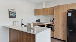 Eine moderne Küche mit Holzschränken, einem schwarzen Kühlschrank und einer weißen Arbeitsplatte.