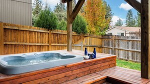 Eine Holzterrasse mit Whirlpool, Holzzaun und Bäumen im Hintergrund.