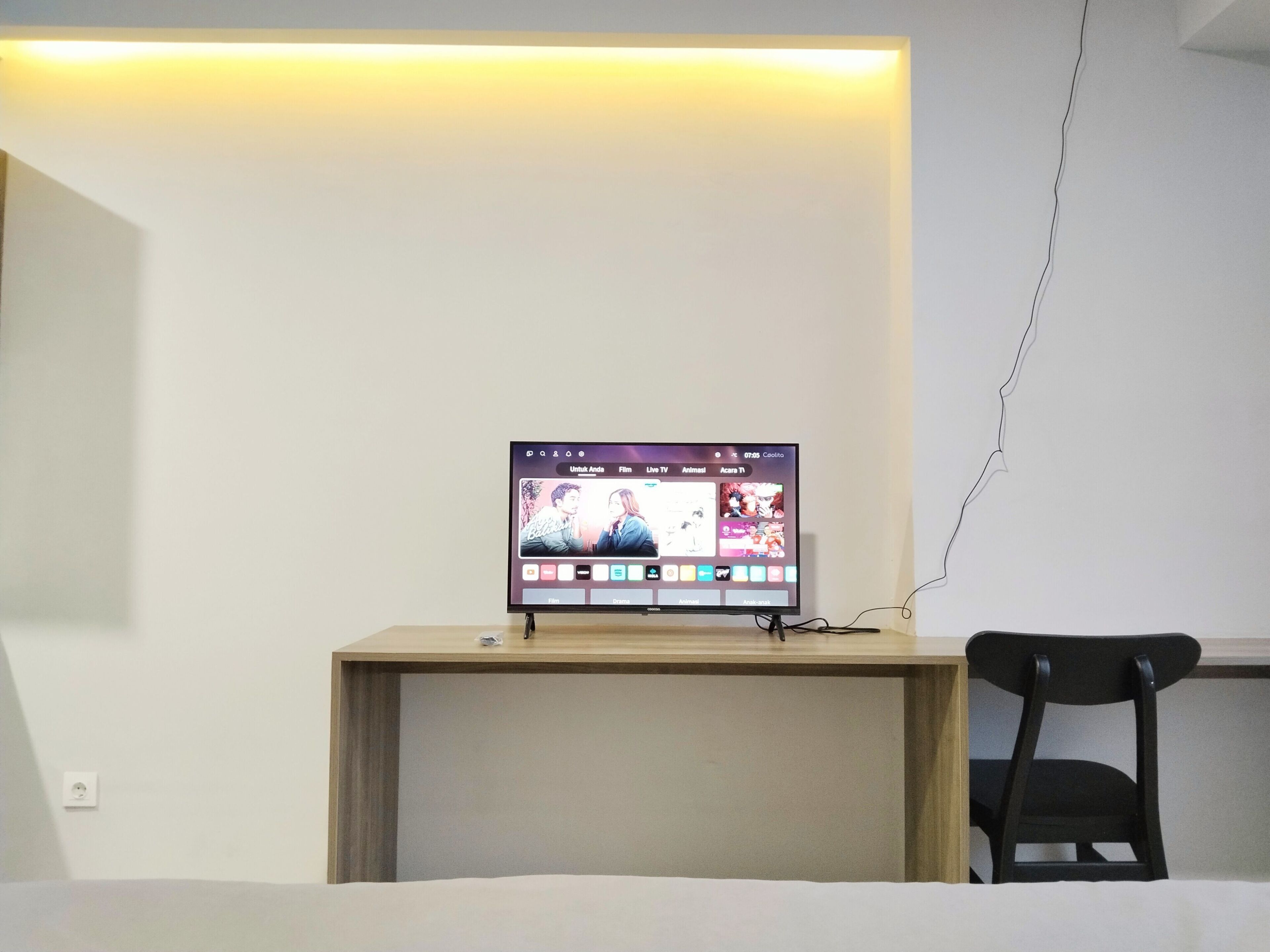 A room with a bed, a desk with a computer monitor displaying a streaming service interface, and a chair.