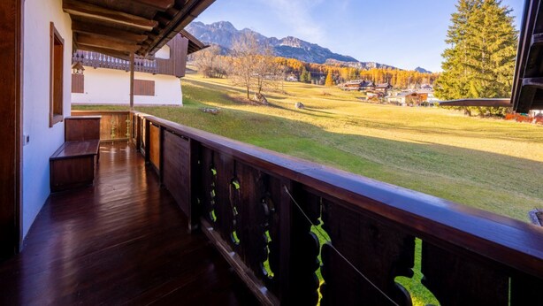 Un balcón de madera con vistas a un campo cubierto de hierba y montañas.