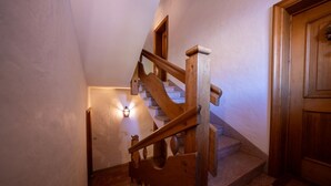 Una escalera de madera con barandilla, una lámpara en la pared y una puerta de madera.