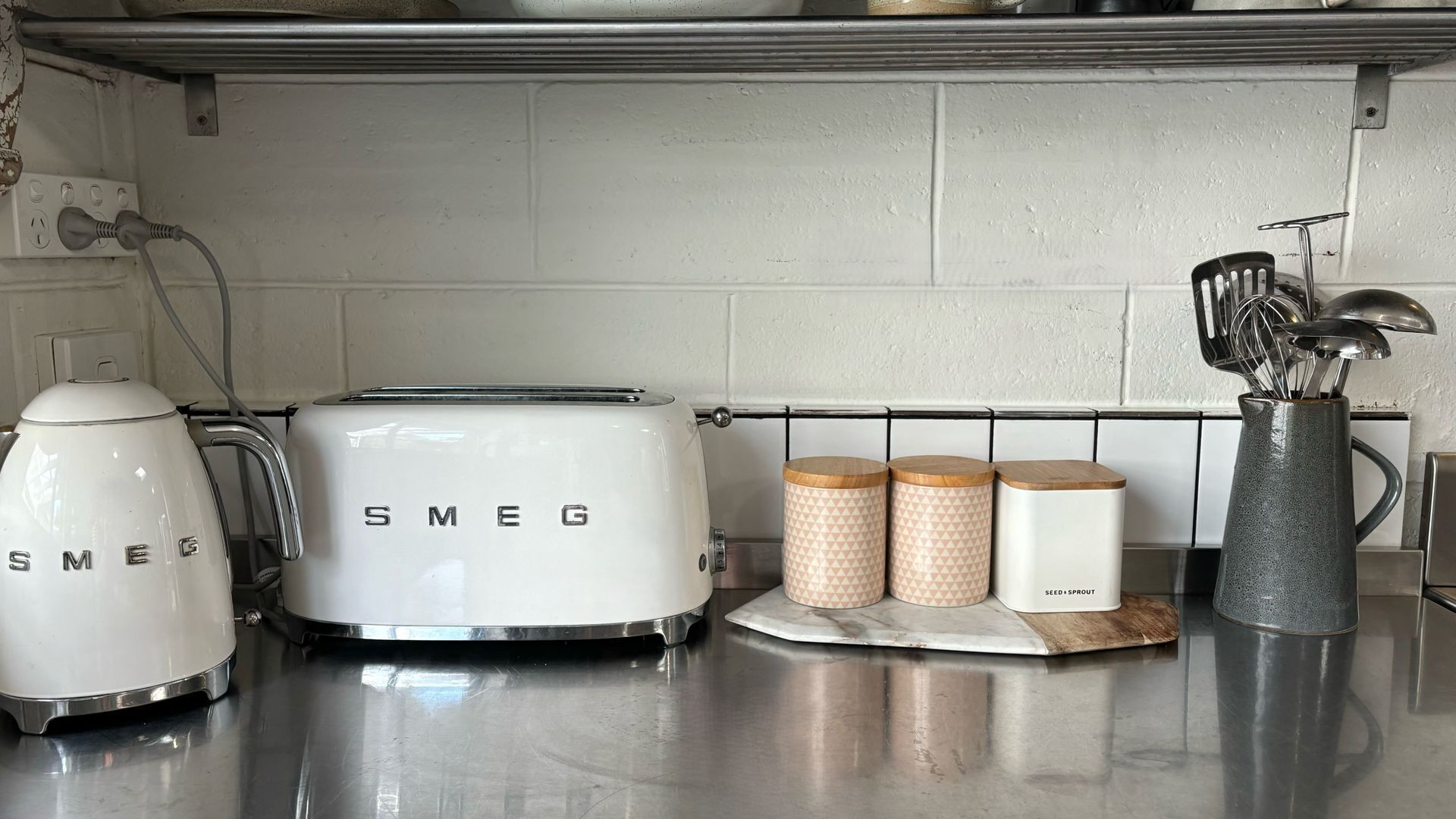 Una cocina con un tostador Smeg blanco, una tetera y dos recipientes estampados con la etiqueta "SEED & SPROUT".