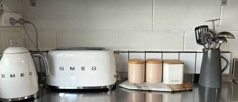 Una cocina con un tostador Smeg blanco, una tetera y dos recipientes estampados con la etiqueta "SEED & SPROUT".