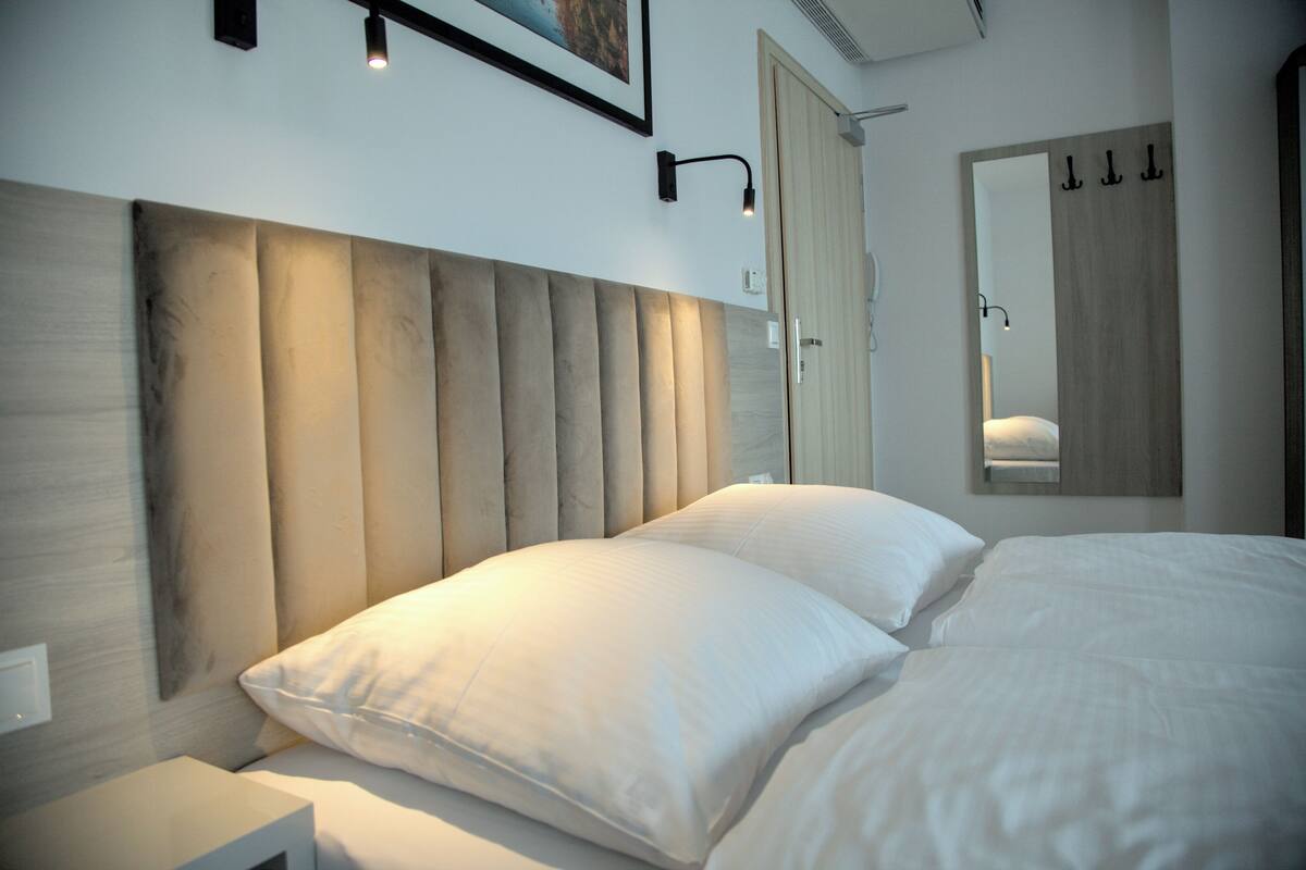 Quarto moderno com cama grande, cabeceira com ripas verticais, mesa de cabeceira, luminária fixada na parede e espelho.