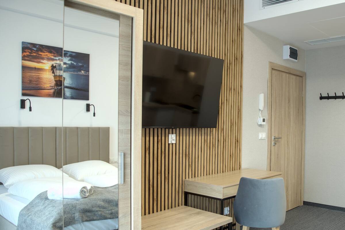 Quarto de hotel moderno com uma cama, escrivaninha, cadeira, televisão e painel de parede de madeira.