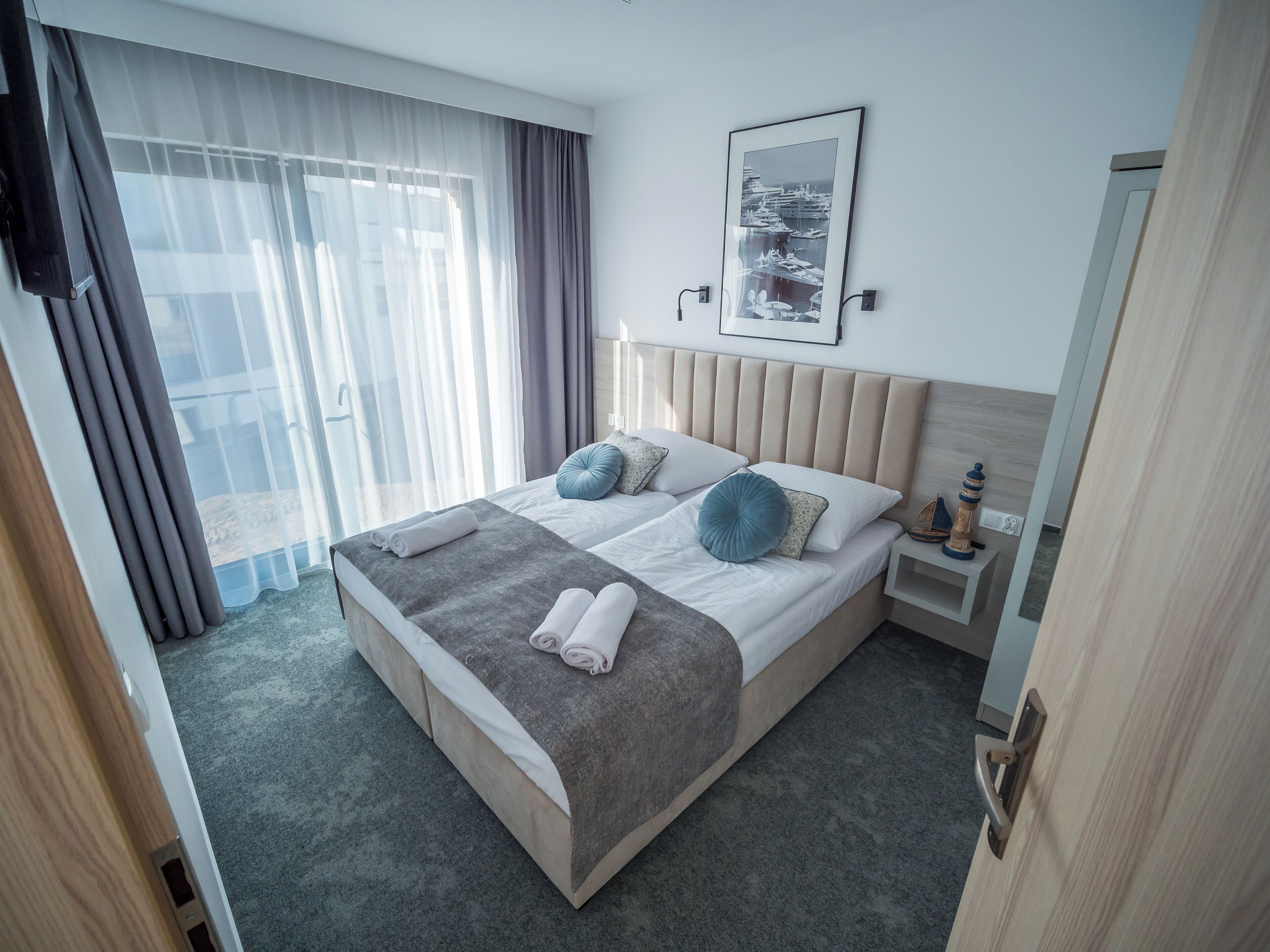 Una habitación de hotel con una cama grande, una mesita de noche y una ventana con cortinas traslúcidas.