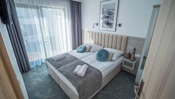 Una habitación de hotel con una cama grande, una mesita de noche y una ventana con cortinas traslúcidas.