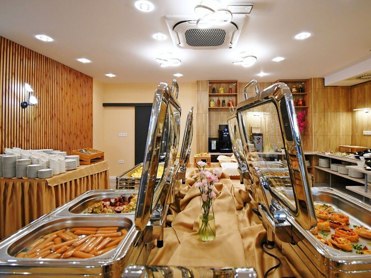 Un buffet avec plusieurs présentoirs de nourriture, une composition florale centrale et un espace cuisine en arrière-plan.