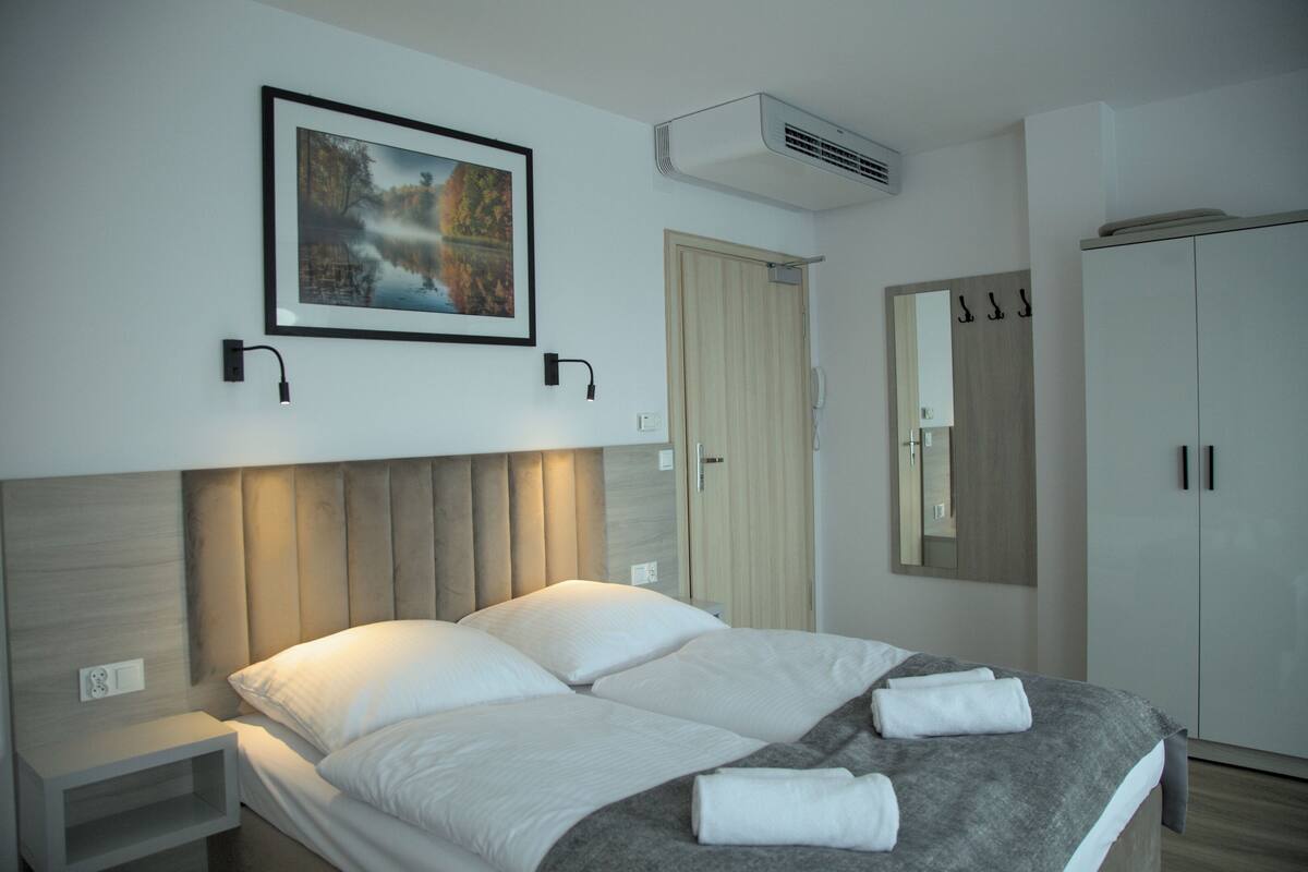 Quarto de hotel moderno com uma cama grande, uma mesa de cabeceira, um guarda-roupa, um espelho e um quadro pendurado na parede.