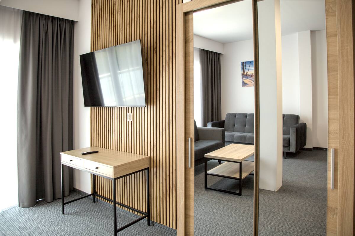Quarto de hotel moderno com uma parede de destaque em madeira, TV de tela plana, escrivaninha com cadeira, sofá e mesa de centro.