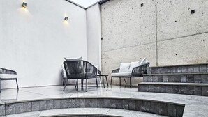 Ett modernt utomhusområde med sittplatser, bestående av en böjd bänk i sten, två stolar och en soffa.