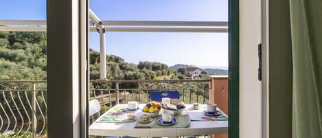 An outdoor dining area with a table set for two, a blue chair, and a view of a hilly landscape.