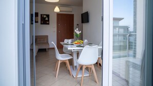 A modern dining area with a table set for two, a sofa, and a TV mounted on the wall.