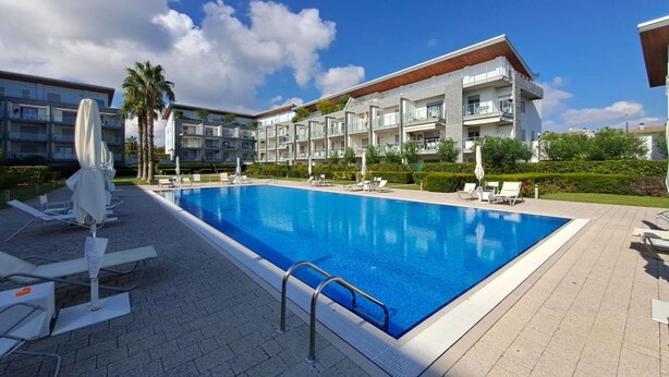 A swimming pool with lounge chairs and umbrellas, surrounded by a modern apartment complex.