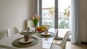 A dining area with a table set for two, a vase of flowers, and a fruit bowl.