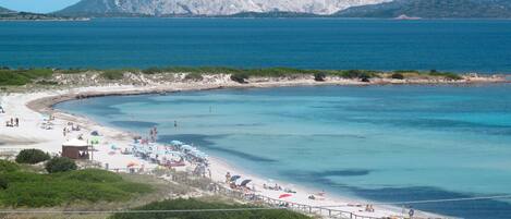 A coastal beach with clear waters, a sandy shore, and a mountainous backdrop.