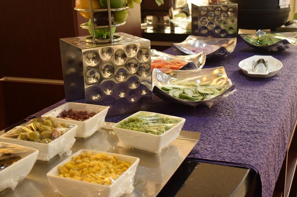 Buffet com diversos alimentos, incluindo azeitonas, ervilhas verdes e pepinos fatiados.