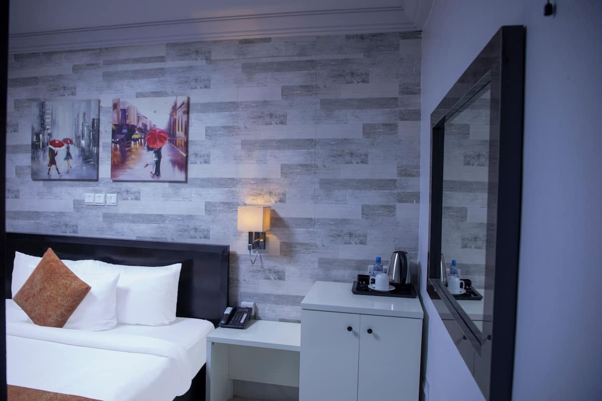 A hotel room with a bed, a nightstand, a desk, a cabinet, a wall-mounted lamp, and two framed pictures on the wall.