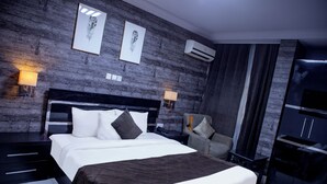 A modern hotel room with a large bed, a dark wood accent wall, two wall-mounted lamps, and a built-in TV. - NewLand Hotels and Apartments (Abuja)