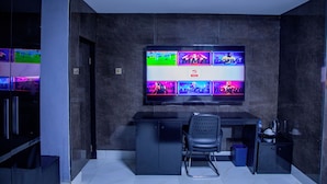 A modern room with a large TV displaying various sports channels, a desk with a chair, and a small cabinet. - NewLand Hotels and Apartments (Abuja)