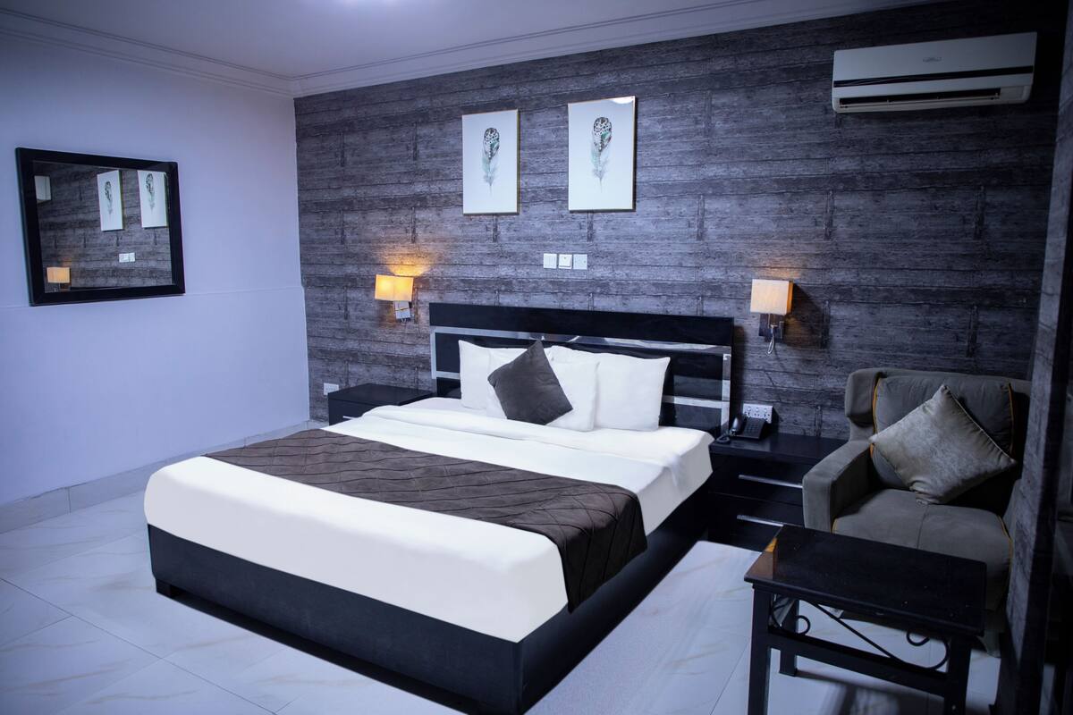 A modern hotel room with a large bed, bedside tables, a sofa, and artwork on the wall.