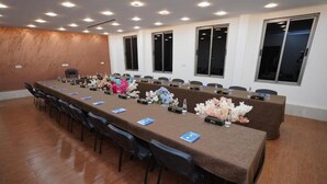 A conference room with a long table, chairs, nameplates, and floral centerpieces. - NewLand Hotels and Apartments (Abuja)