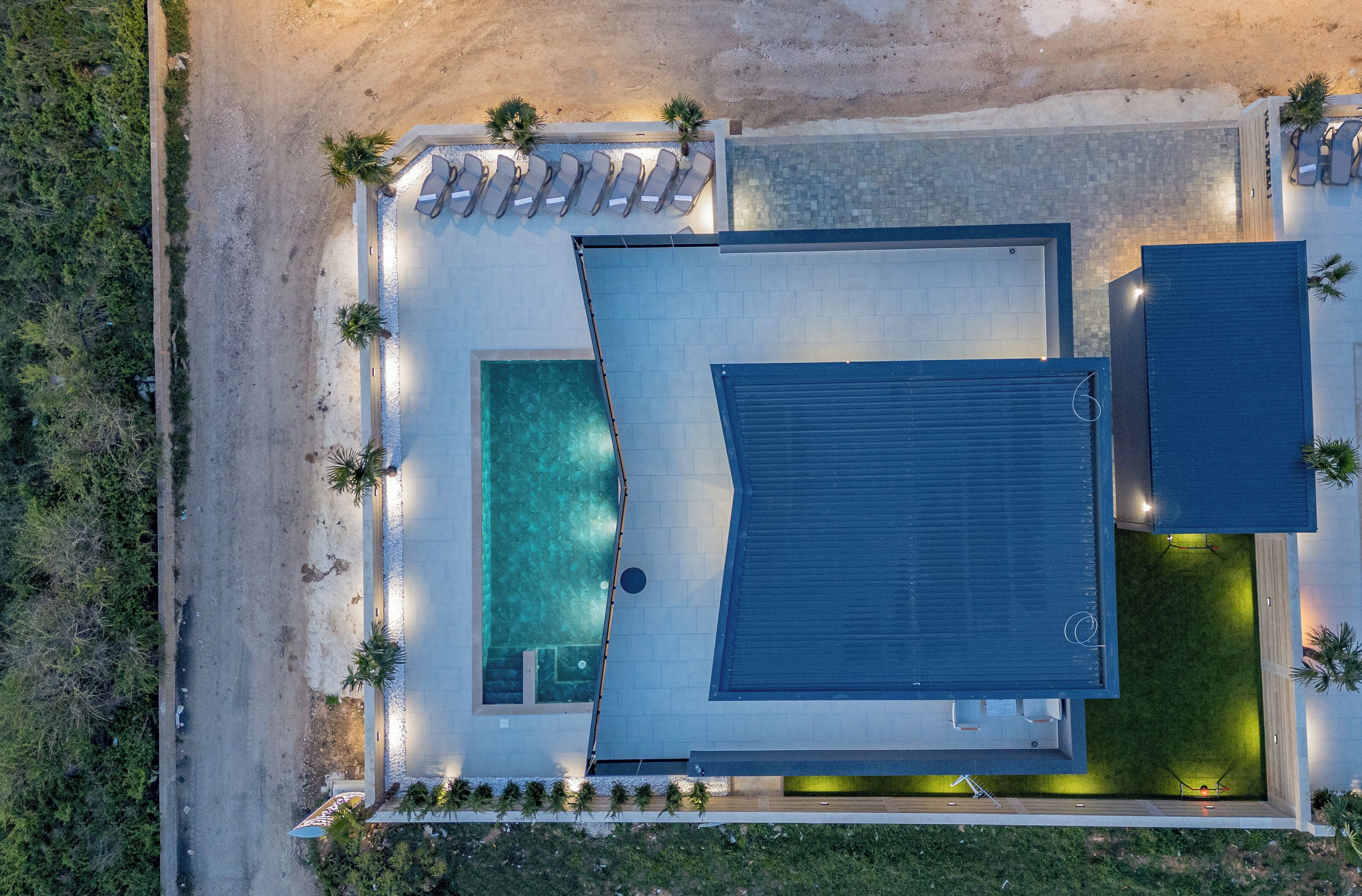 Vista aérea de un moderno complejo turístico con piscina, un porche cubierto y una amplia terraza.