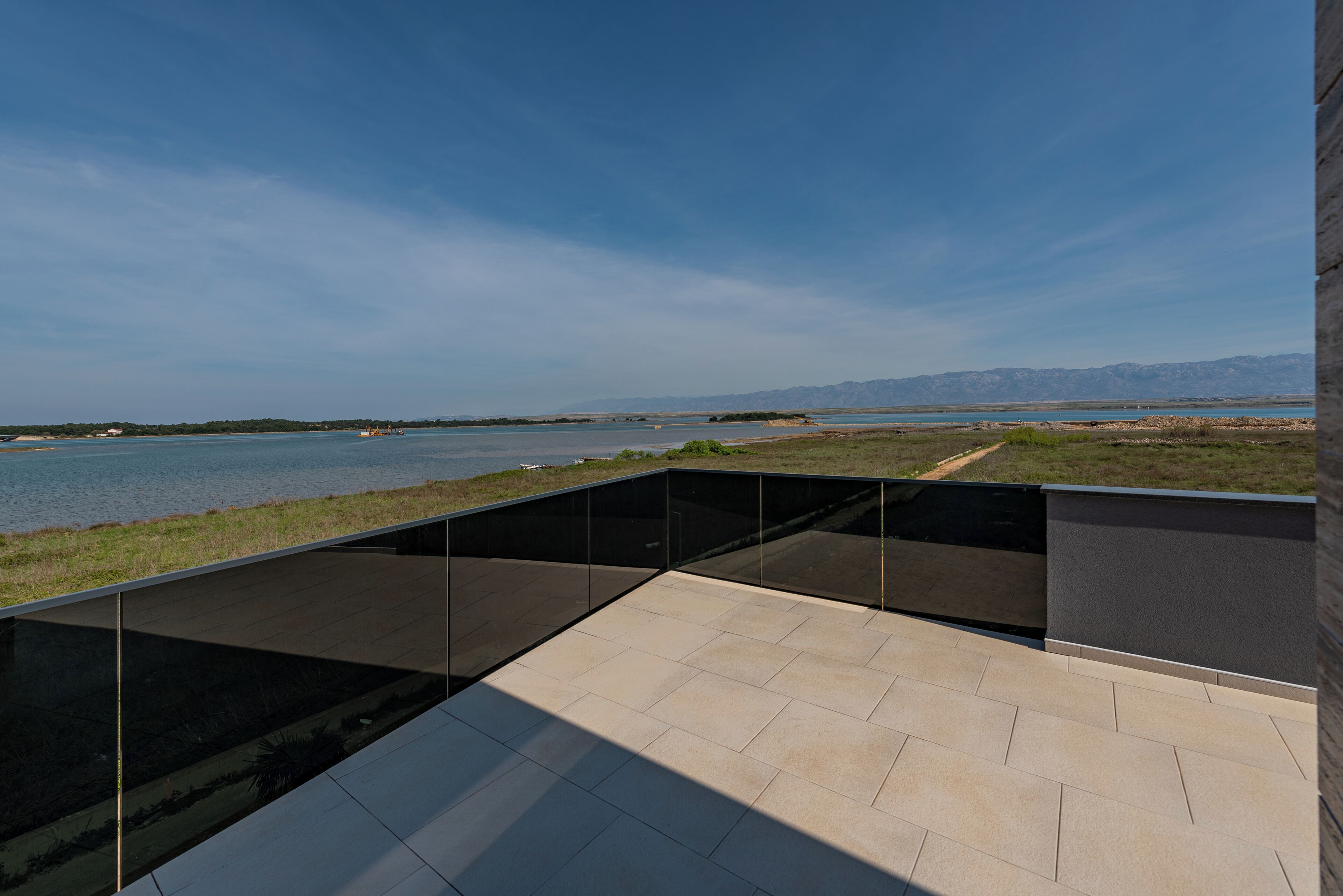 Eine moderne Terrassenanlage mit Blick auf ruhiges Gewässer und ferne Berge.
