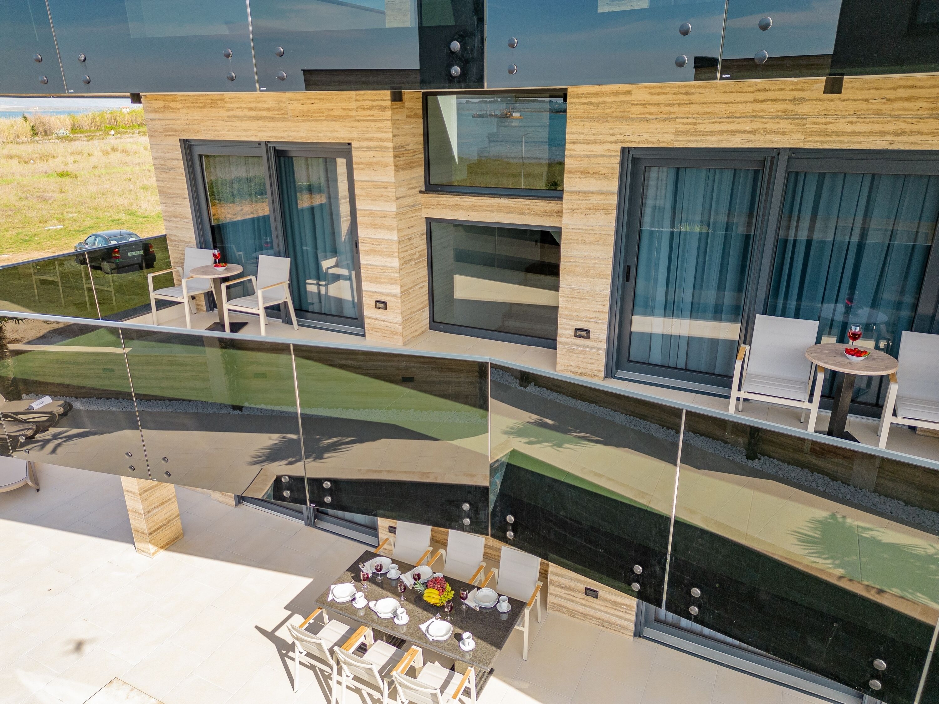 A modern hotel room with a glass balcony, a dining area with a table set for four, and a view of the surrounding landscape.