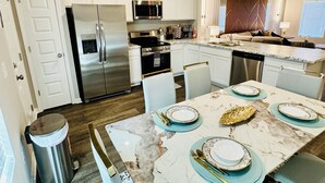 A modern kitchen with stainless steel appliances, a dining area with a marble table, and a small island. - Comfort house weekly discount and monthly discount (Cullman)