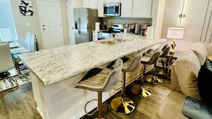 A modern kitchen with a large island, stainless steel appliances, and a bar area with stools. - Comfort house weekly discount and monthly discount (Cullman)