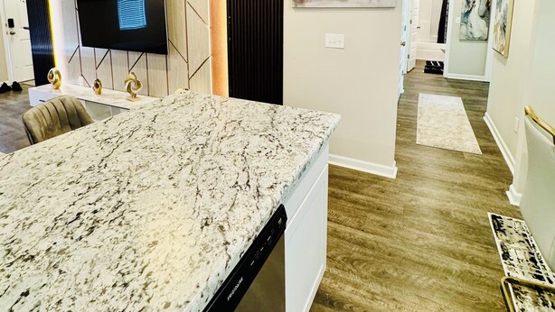 A modern kitchen with a marble countertop, built-in appliances, and a flat-screen TV mounted on the wall. - Comfort house weekly discount and monthly discount (Cullman)