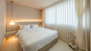 A modern bedroom with a large bed, a bedside table, a wall-mounted light, and sheer curtains. - Busan Ji Villard Pension (Busan)