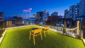 A rooftop terrace with artificial grass, two yellow chairs, and a cityscape view at dusk. - Busan Ji Villard Pension (Busan)