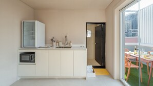 A compact kitchen with a microwave, sink, and cabinets, leading to a balcony with a table and chairs. - Busan Ji Villard Pension (Busan)
