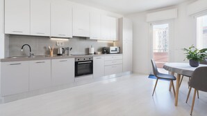 A modern kitchen with white cabinets, a built-in oven, and a dining area with a table and chairs.