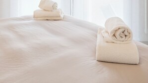 A hotel room with a large bed, two windows, and two rolled towels on the bed.