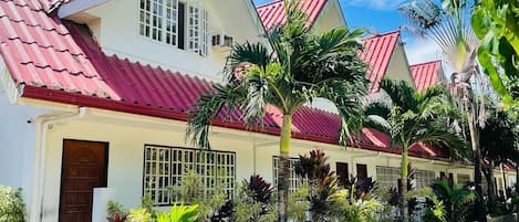 A two-story building with a red-tiled roof, white walls, and a gated entrance.