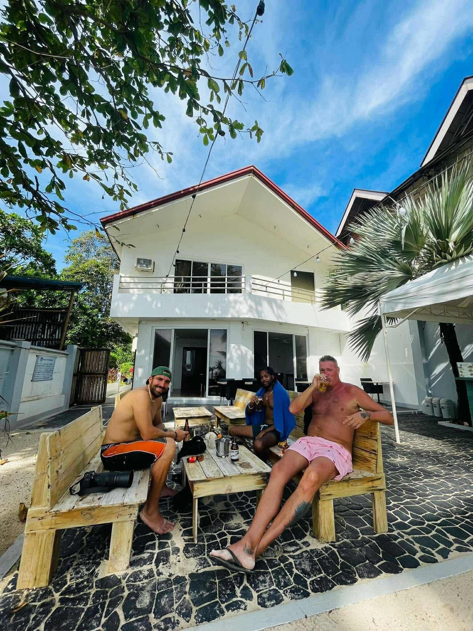 Una casa con fachada blanca y techo rojo, terraza de madera y patio con baldosas.