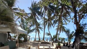 An outdoor seating area with wooden tables and benches, surrounded by palm trees, overlooking a beach. - Castle Rock Boracay (Boracay Island)
