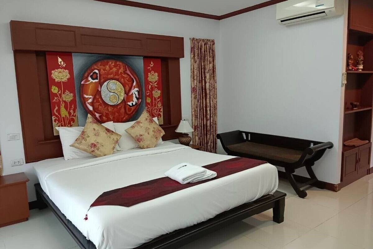 Una cama bien hecha con una colcha rojo y blanco, un almohadón con estampado floral y un tapiz decorativo encima.