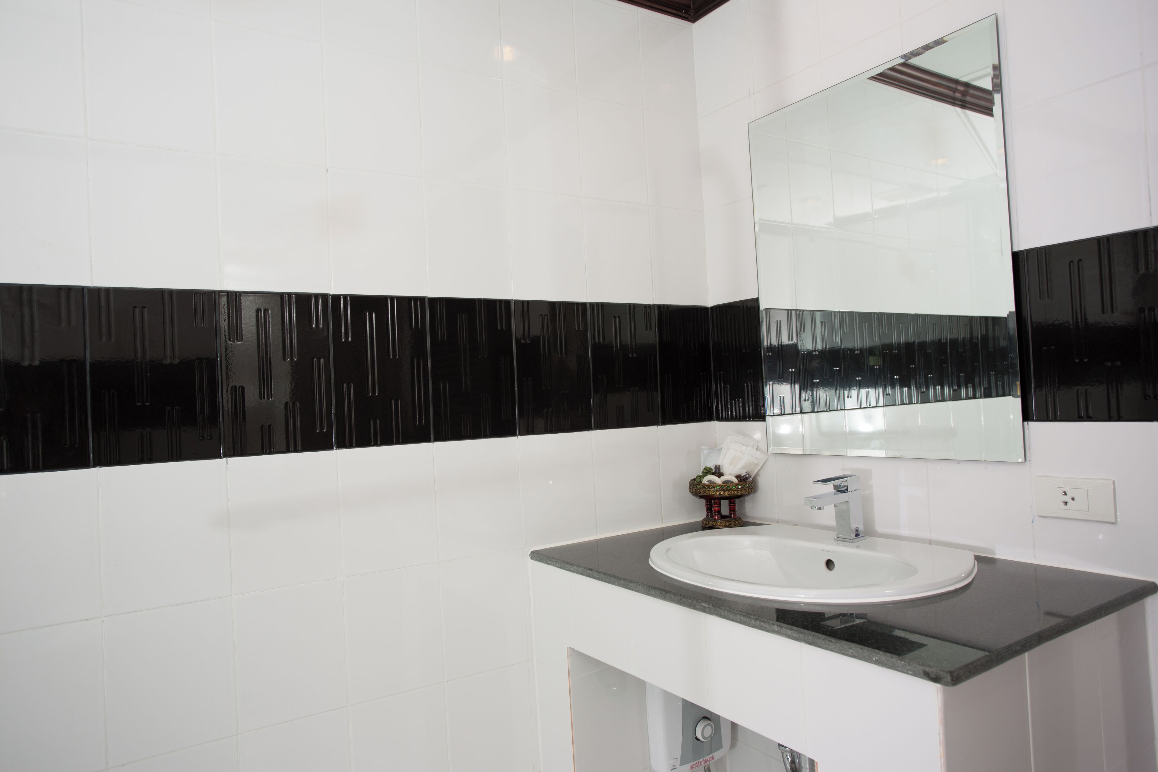 Un baño moderno con un lavamanos blanco, paredes con azulejos blanco y negro, y un espejo grande.
