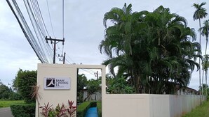 Segnaletica per Baan Chong FA Resort, ingresso con cancello e vialetto che conduce alla proprietà, circondata da vegetazione lussureggiante e palme.
