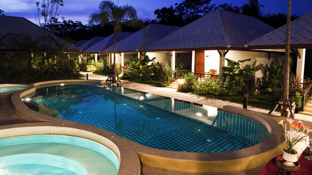 Area piscina con diverse vasche idromassaggio, circondata da bungalow sull'acqua con tetti in tegole.