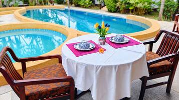 A poolside dining area with a table set for two, surrounded by chairs with patterned cushions.