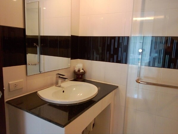 A bathroom with a white sink, black countertop, and a glass shower enclosure. - BAANCHONGFA RESORT (Takua Pa)