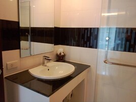 Un baño con lavamanos blanco, encimera negra y cabina de ducha de vidrio.