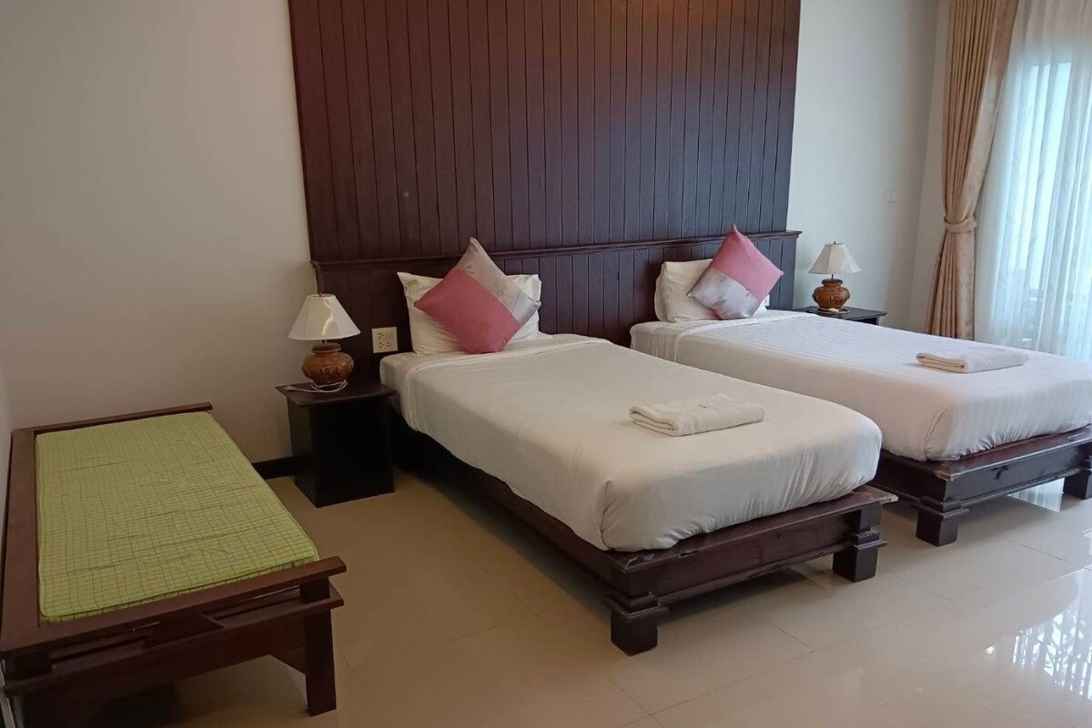 Een hotelkamer met twee bedden, een nachtkastje met een lamp, een houten tafel met een groene onderzetter en een houten hoofdbord.