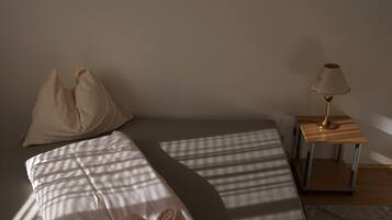 A neatly made bed with pillows and a rolled towel, a bedside lamp, and a small wooden nightstand.