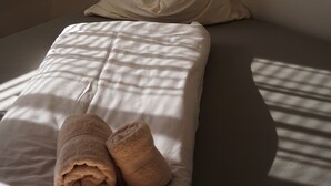 Una cama con una colcha blanca y dos toallas enrolladas.